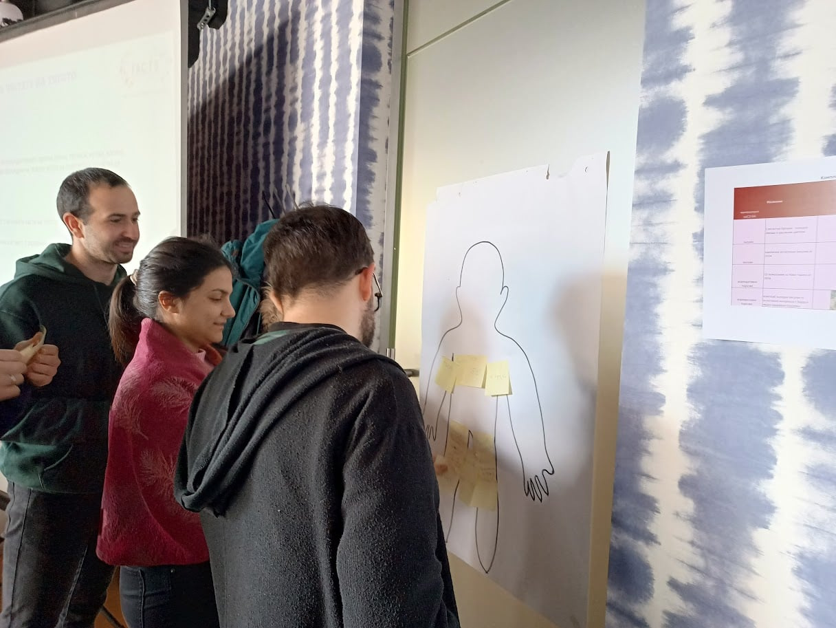 Three teacher trainers during a pilot training session for the FACTS project. They are attaching labels to a drawing of the outline of a human body